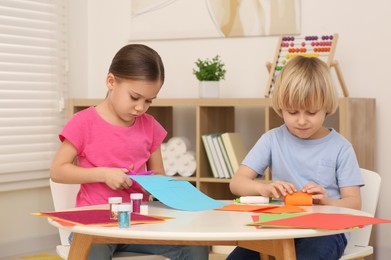 Photo of Cute children cutting colorful paper at desk in room. Home workplace