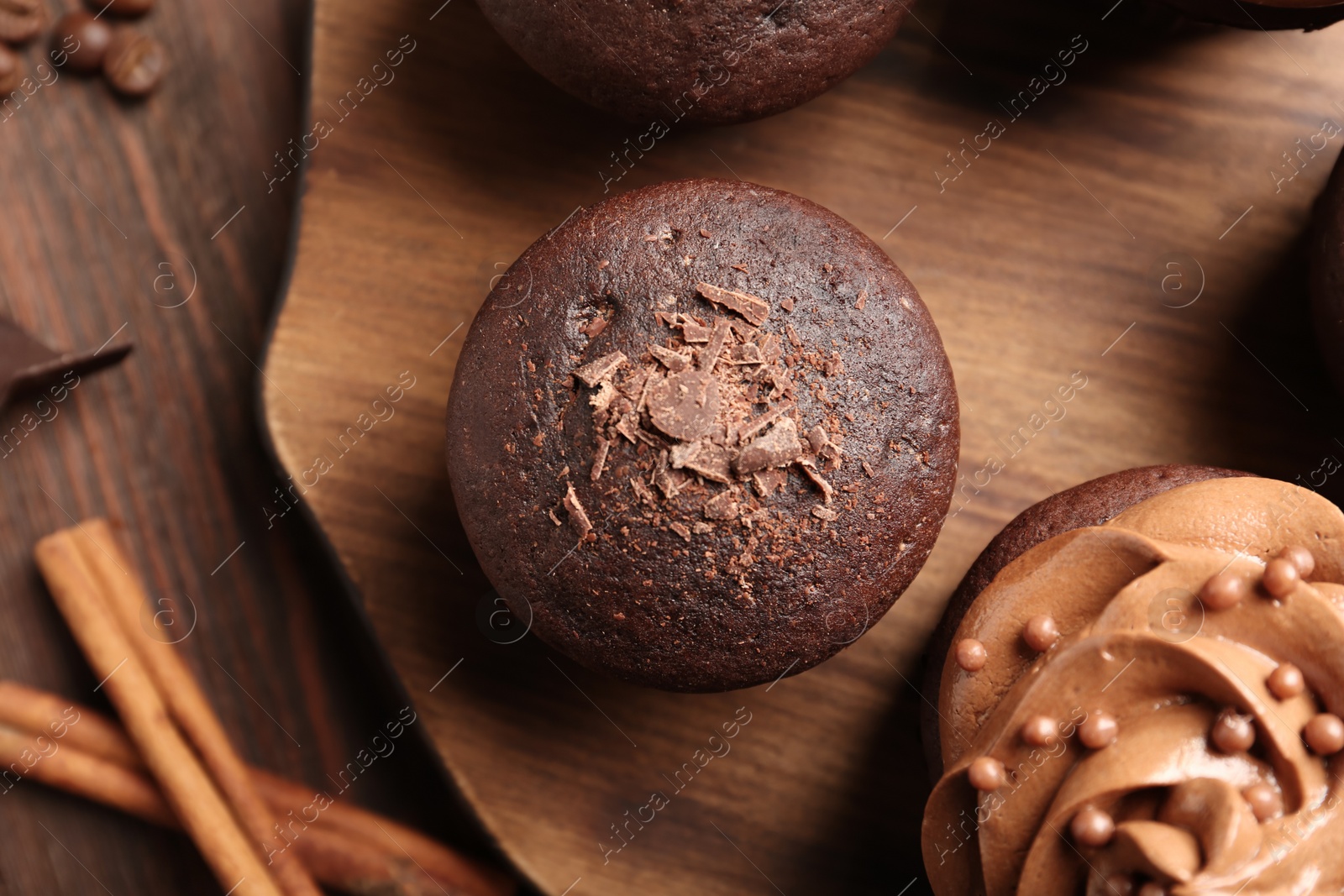 Photo of Delicious chocolate muffin and cupcake decorated with cream on wooden table, flat lay