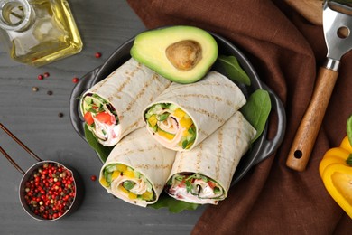 Photo of Delicious sandwich wraps with fresh vegetables, peppercorns, avocado and oil on grey wooden table, flat lay