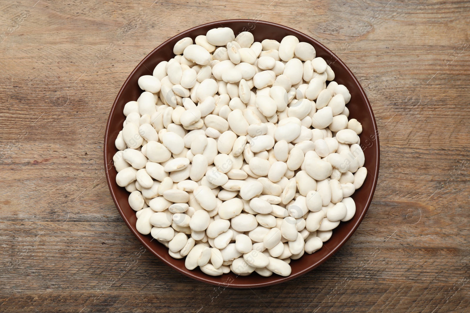Photo of Raw white beans in bowl on wooden table, top view