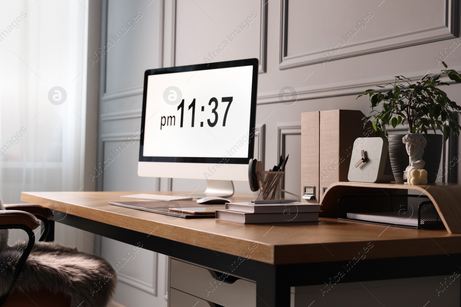 Photo of Stylish workplace with computer, houseplant and stationery on wooden desk near grey wall at home