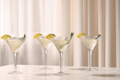 Elegant martini glasses with fresh cocktail, rosemary and lemon slices on white table indoors