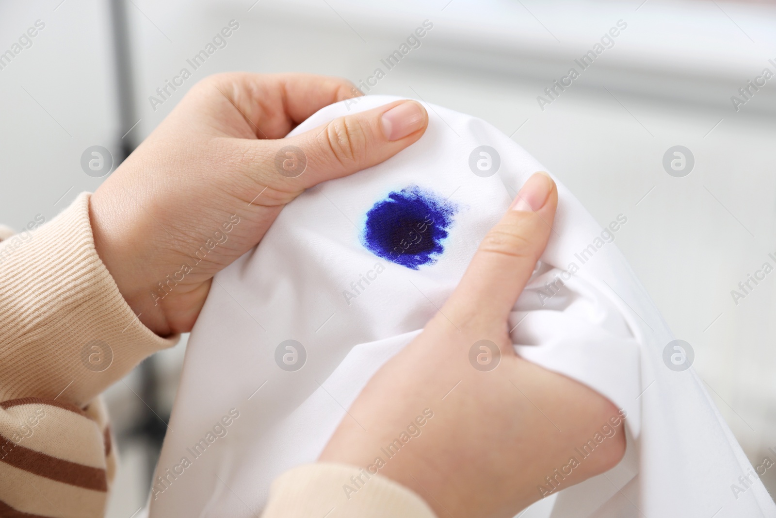 Photo of Woman holding white shirt with blue ink stain on blurred background, closeup