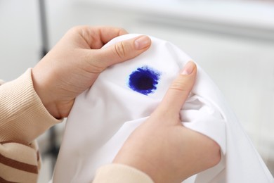 Photo of Woman holding white shirt with blue ink stain on blurred background, closeup