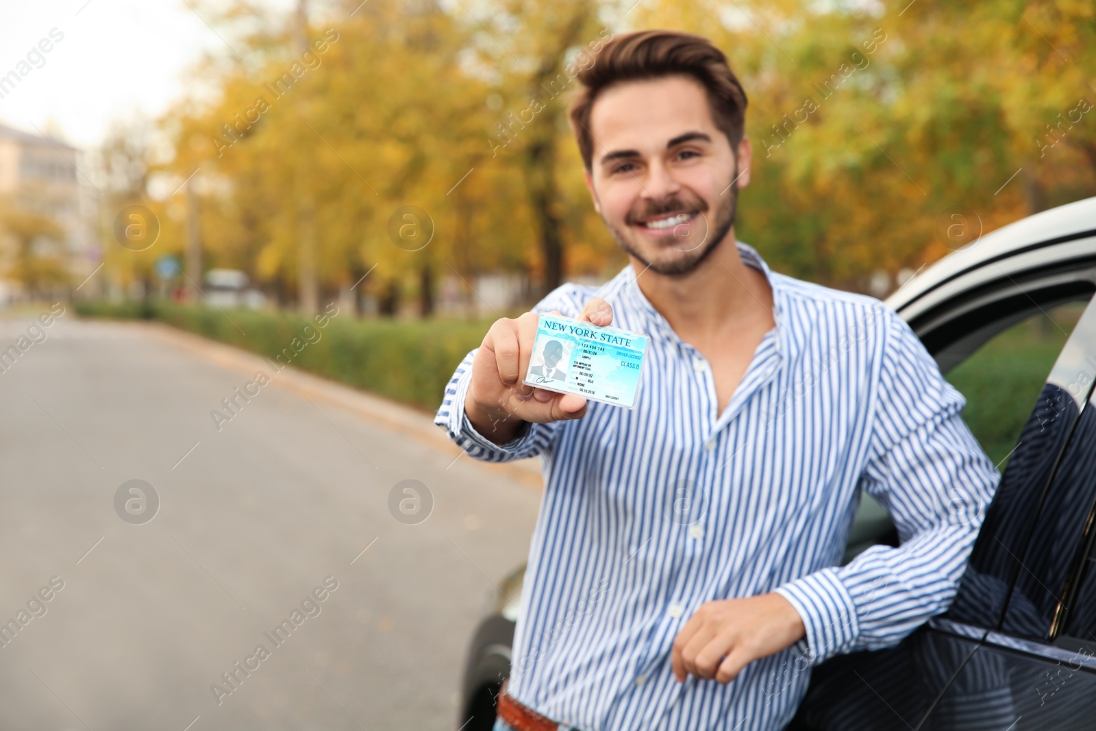 Photo of Young man holding driving license near open car. Space for text