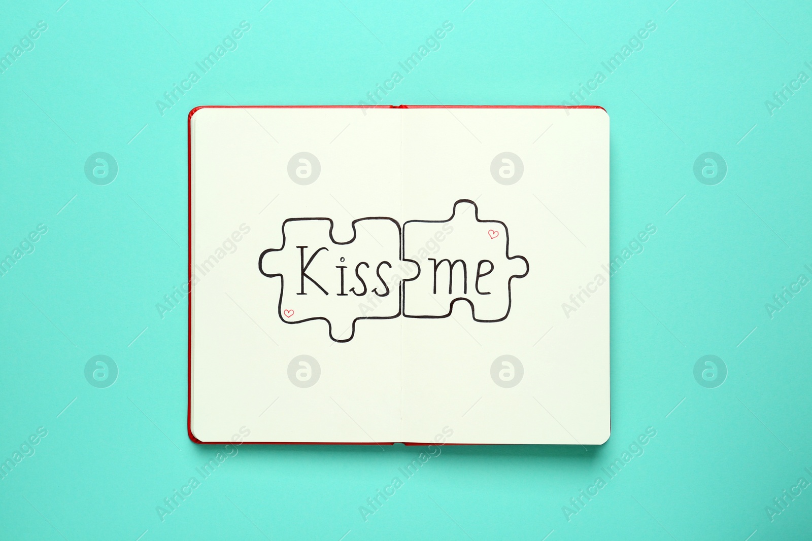 Photo of Open notebook with phrase Kiss Me and drawn puzzles on turquoise background, top view