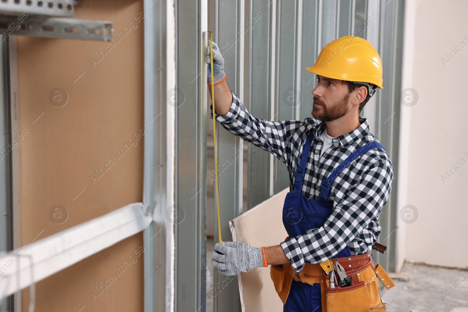 Photo of Professional builder in uniform working with measuring tape indoors