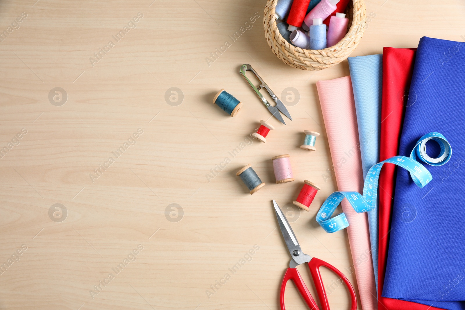 Photo of Set of sewing supplies and accessories on wooden table, flat lay. Space for text