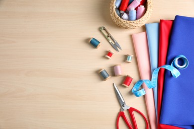 Set of sewing supplies and accessories on wooden table, flat lay. Space for text