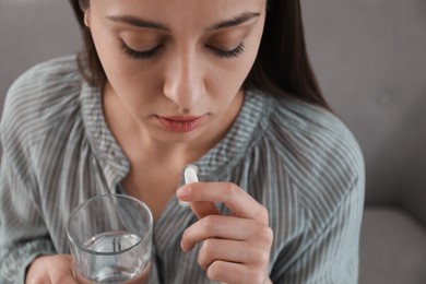Photo of Young woman taking abortion pill on sofa, closeup