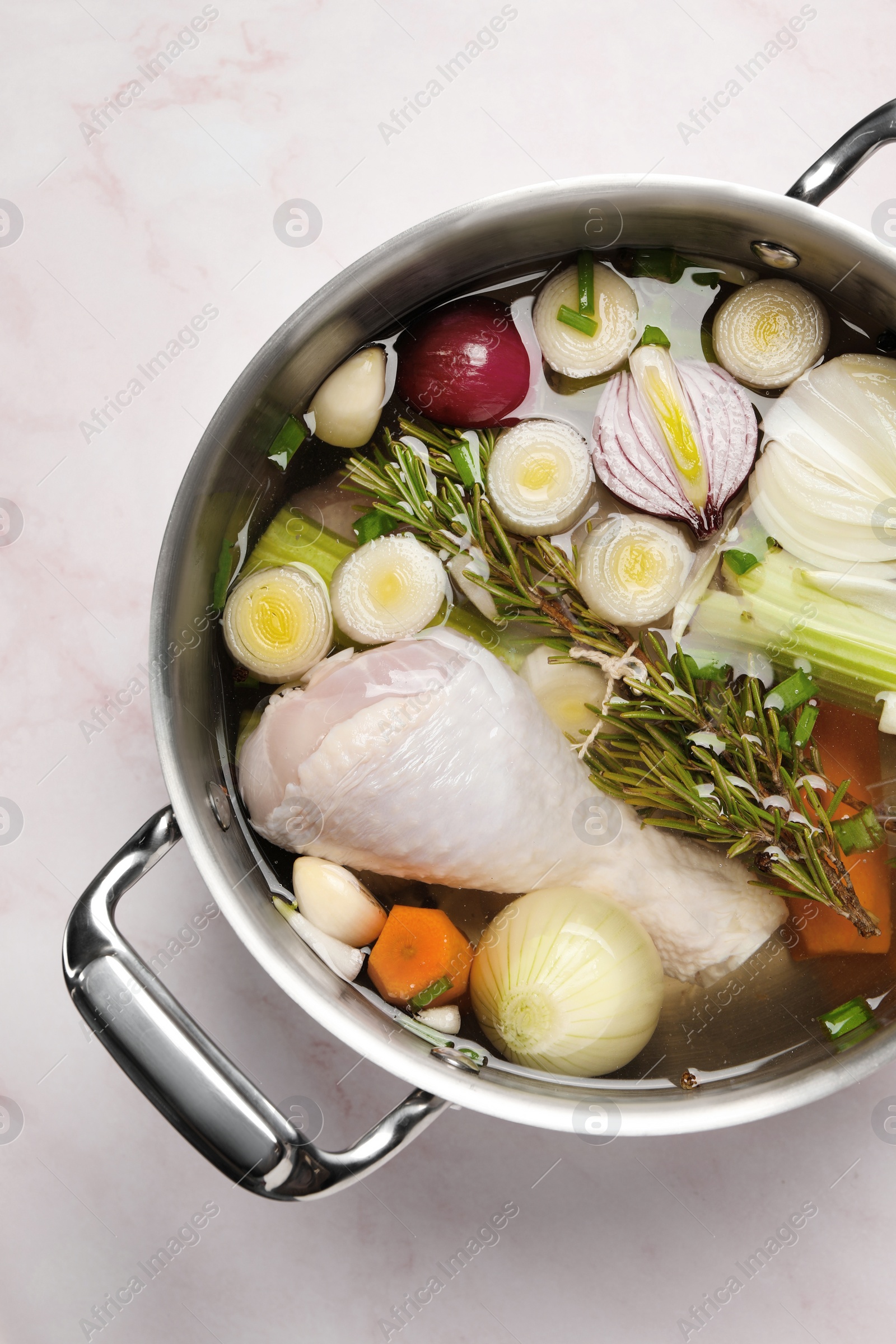 Photo of Different ingredients for cooking tasty bouillon in pot on pink marble table, top view