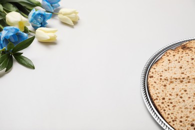 Photo of Tasty matzos and fresh tulips on light grey background, space for text. Passover (Pesach) celebration