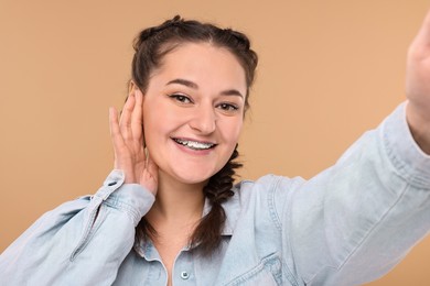 Photo of Smiling woman with braces taking selfie on beige background