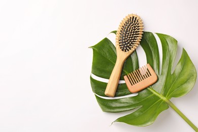 Photo of Wooden hairbrush, comb and green leaf on white background, flat lay. Space for text