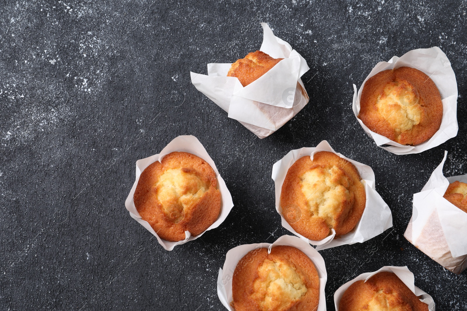 Photo of Delicious sweet muffins on black textured table, flat lay. Space for text