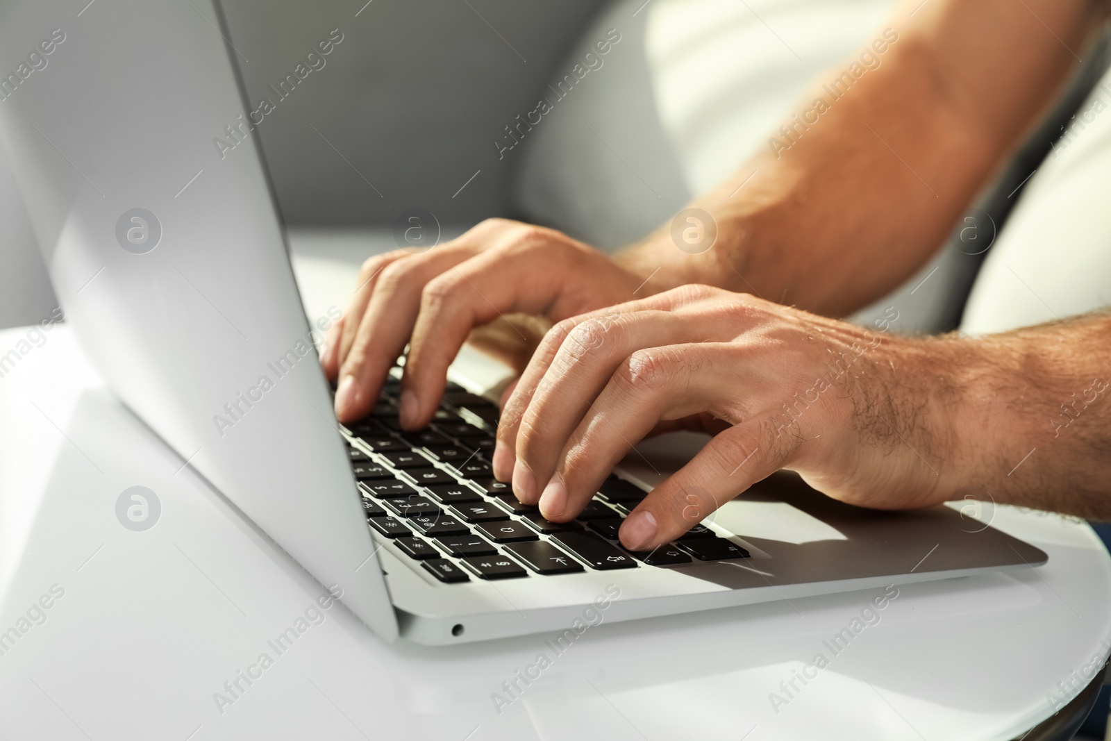 Photo of Man using laptop for search at white table indoors, closeup