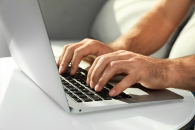 Photo of Man using laptop for search at white table indoors, closeup