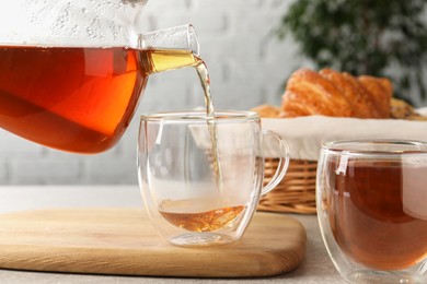 Pouring aromatic tea into glass cup at table, closeup