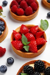 Photo of Tartlets with different fresh berries on white table. Delicious dessert