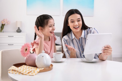 Photo of Mother and daughter using video chat on tablet at table indoors