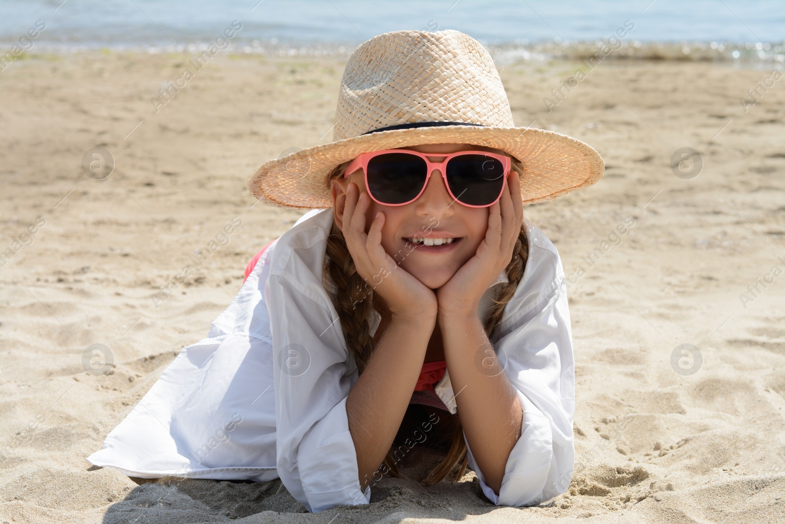 Photo of Little girl wearing sunglasses and hat at beach on sunny day