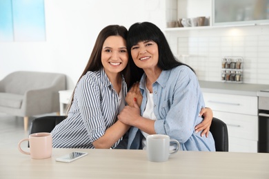 Photo of Portrait of young woman and her mature mother at table indoors