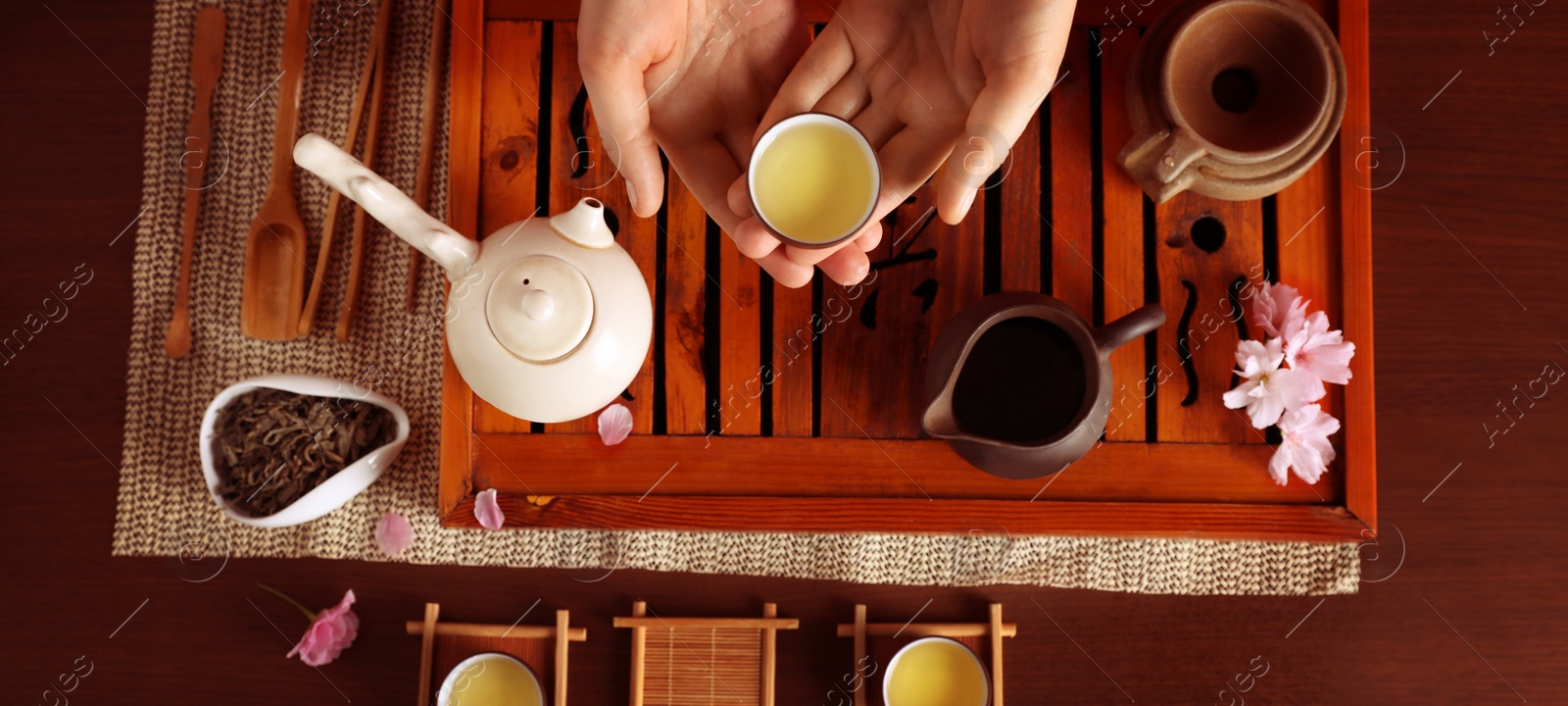 Image of Woman with cup of freshly brewed tea during traditional ceremony at wooden table, top view. Banner design