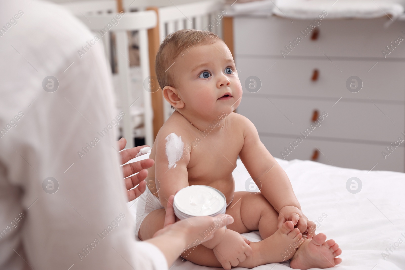 Photo of Mother applying moisturizing cream on her little baby at home, closeup