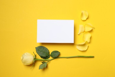 Photo of Beautiful rose, petals and blank card on yellow background, flat lay. Space for text