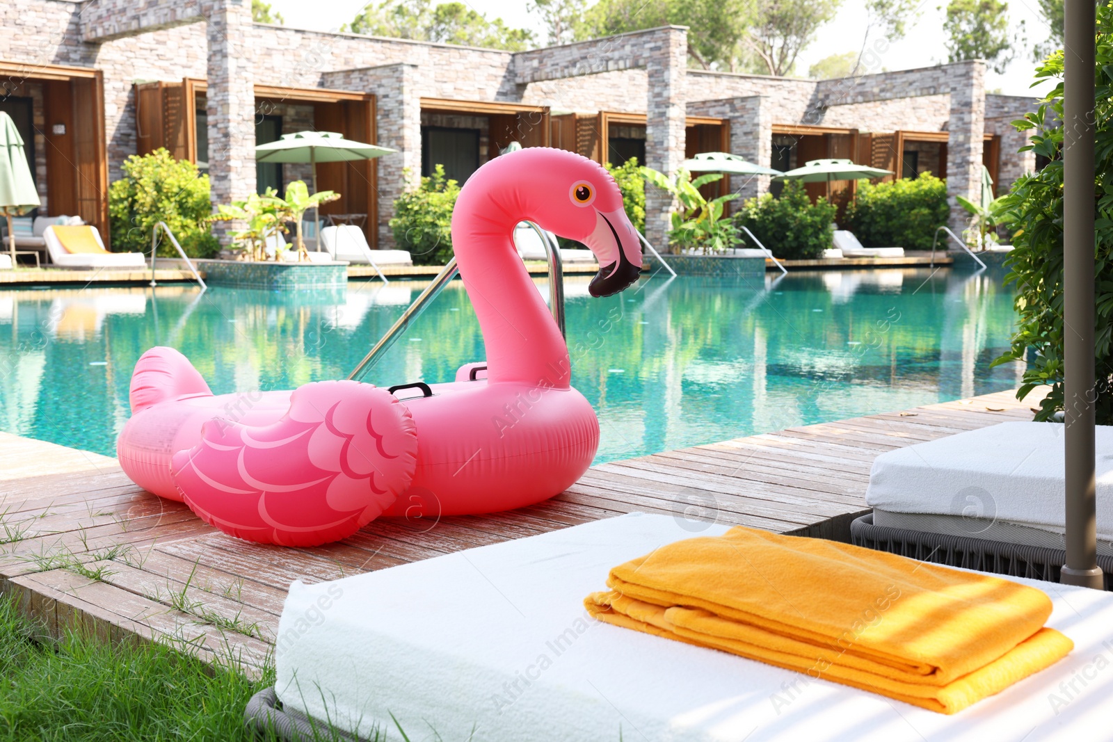 Photo of Float in shape of flamingo on wooden deck near swimming pool and sunbeds at luxury resort
