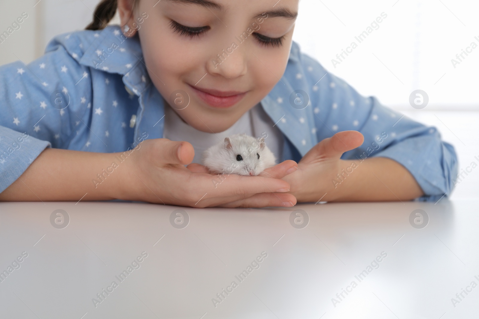 Photo of Little girl with cute hamster at table indoors