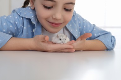 Little girl with cute hamster at table indoors