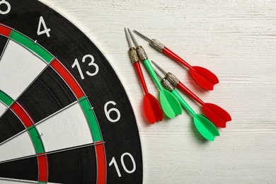 Dart board with color arrows on white wooden background, top view