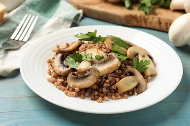 Tasty buckwheat with fresh parsley, mushrooms and fork on light blue wooden table, closeup