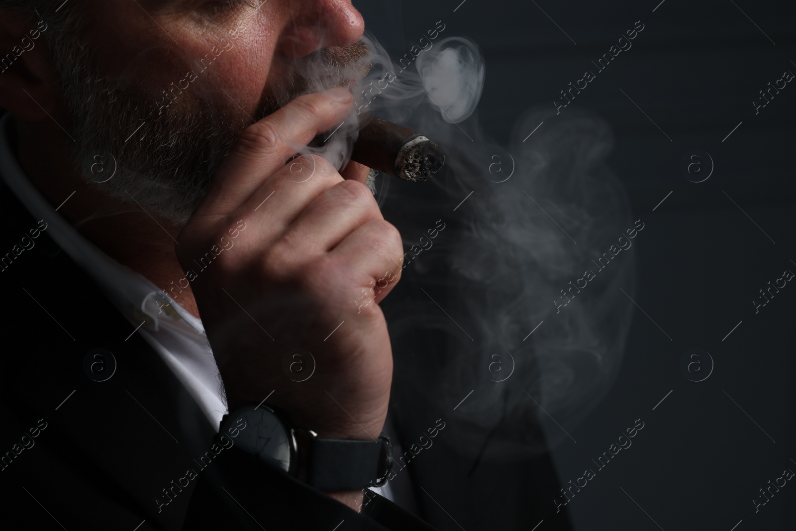 Photo of Bearded man smoking cigar against dark grey background, closeup. Space for text