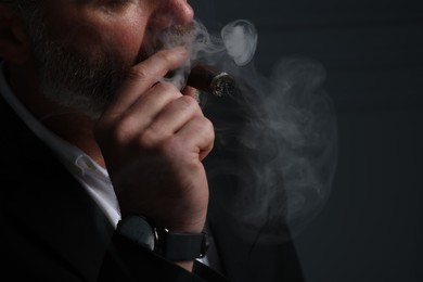 Photo of Bearded man smoking cigar against dark grey background, closeup. Space for text