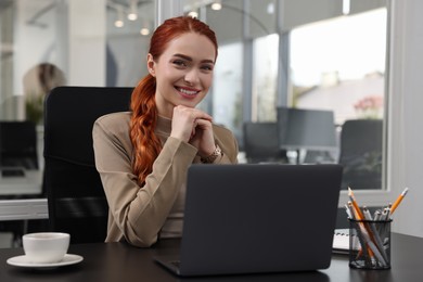 Happy woman working with laptop at black desk in office