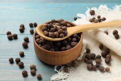 Photo of Aromatic allspice pepper grains in bowl and spoon on light blue wooden table