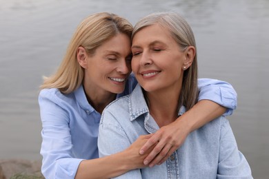 Happy mature mother and her daughter hugging near pond