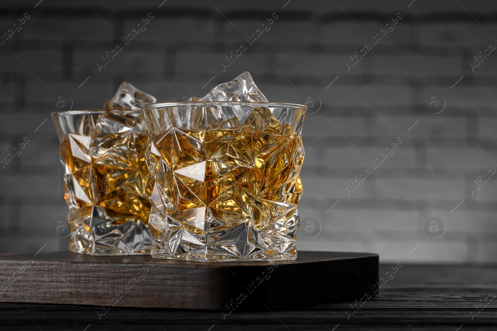 Photo of Whiskey and ice cubes in glasses on black wooden table, closeup. Space for text