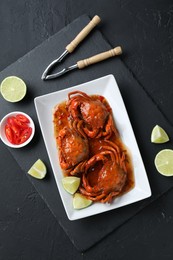 Delicious boiled crabs with sauce and lime served on black textured table, top view