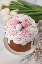 Photo of Tasty Easter cake with decorative sugar eggs and flowers on white marble table, above view