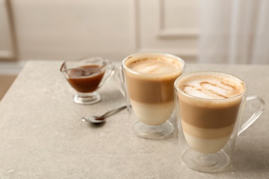 Photo of Glass cups of tasty caramel macchiato and gravy boat with syrup on table. Space for text