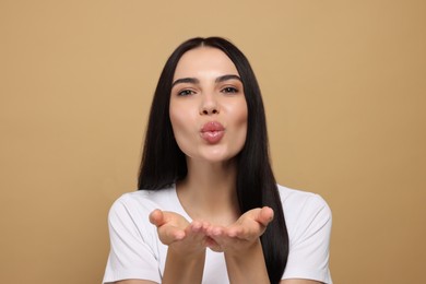Photo of Beautiful young woman blowing kiss on beige background