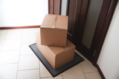 Photo of Cardboard boxes on rug near door. Parcel delivery service