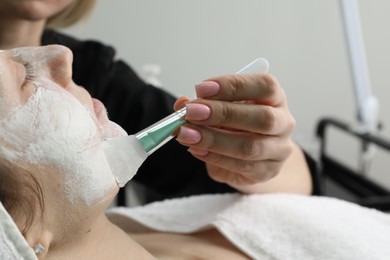 Photo of Cosmetologist applying mask on woman's face in clinic, closeup