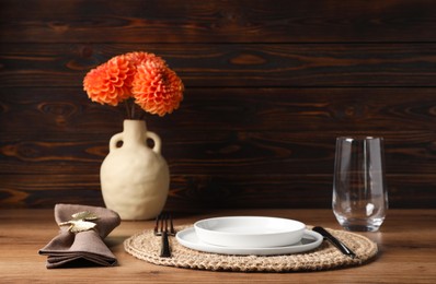 Beautiful cutlery, plate, glass, napkin with ring and flowers in vase on wooden table