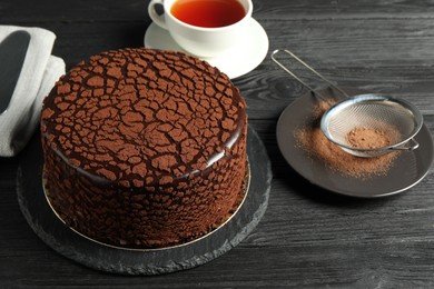 Photo of Delicious chocolate truffle cake, cocoa powder and tea on black wooden table