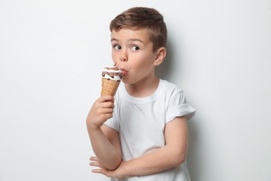 Adorable little boy with delicious ice cream against light background