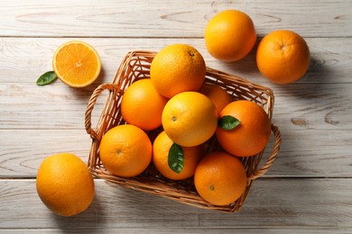 Photo of Many ripe oranges and green leaves on wooden table, top view